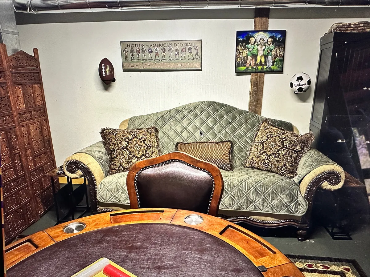 The image highlights a game room with a plush green couch, a poker table, and sports memorabilia on the walls. The space is designed for fun and socializing, ideal for family game nights and making memories together.