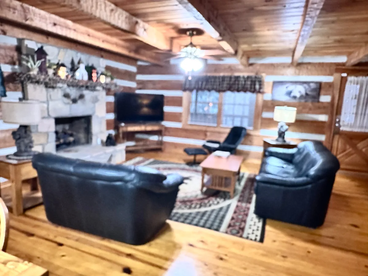 A warm and welcoming living area featuring a stone fireplace, comfortable sofa set, coffee table, and a large window. The ambiance is cozy and intimate, ideal for curling up together after a day of adventure.