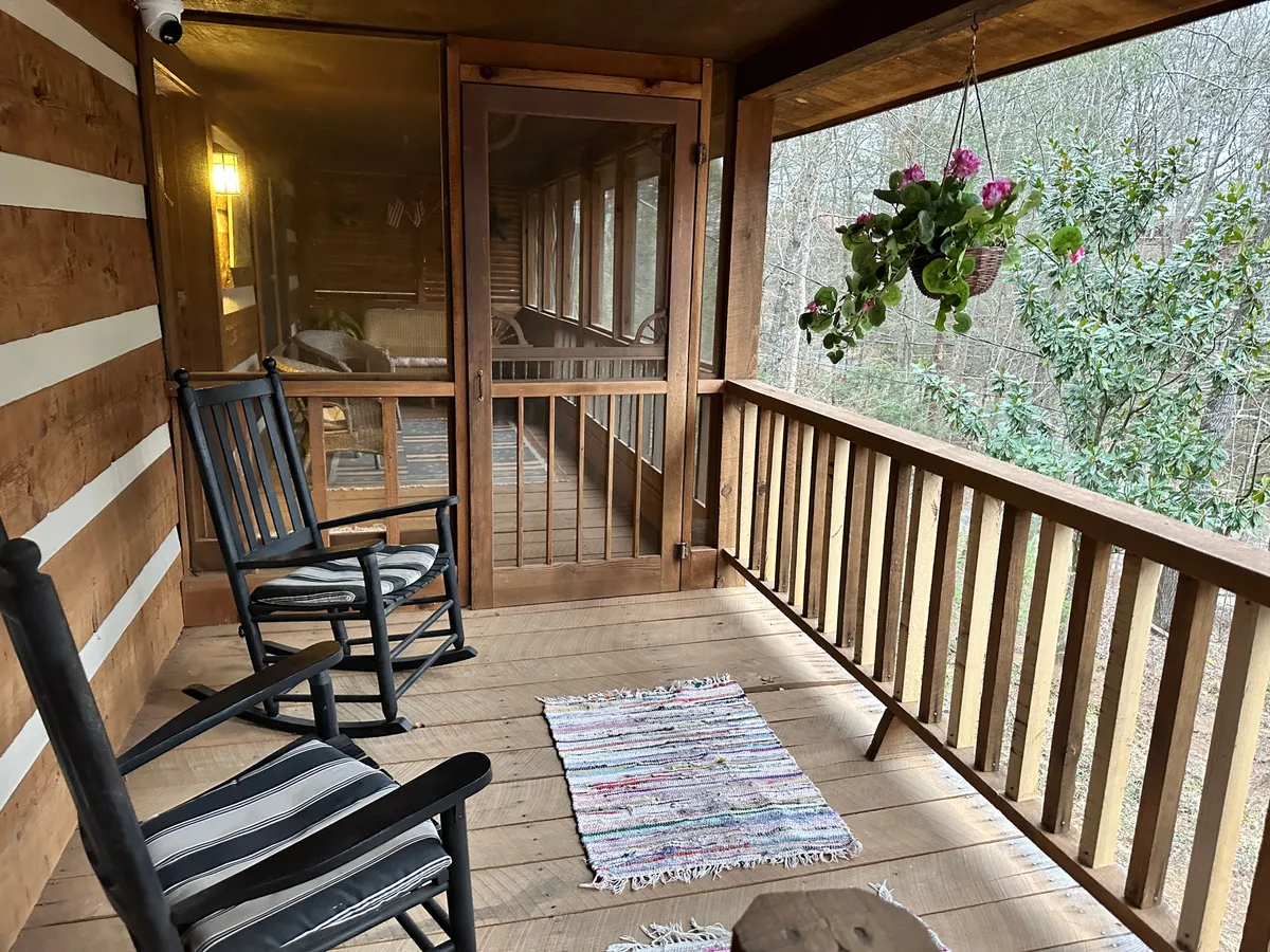 This image features a porch with classic wooden rocking chairs, hanging plants, and a woven rug, overlooking the surrounding nature. The relaxed mood invites guests to unwind and enjoy peaceful moments together outdoors.