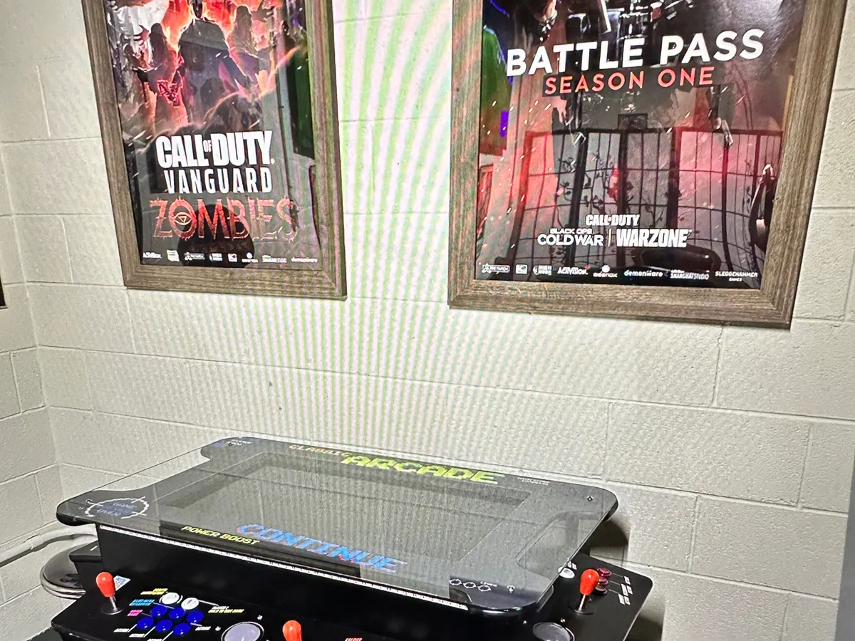 A close-up of an arcade game machine with vibrant posters of video games in the background. The area is designed for competitive play, inviting guests to enjoy classic arcade gaming and friendly tournaments in a lively setting.